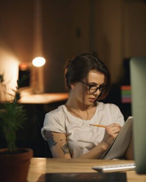 Concentrated young lady designer sitting indoors at night writing notes. Narrativa Conectiva